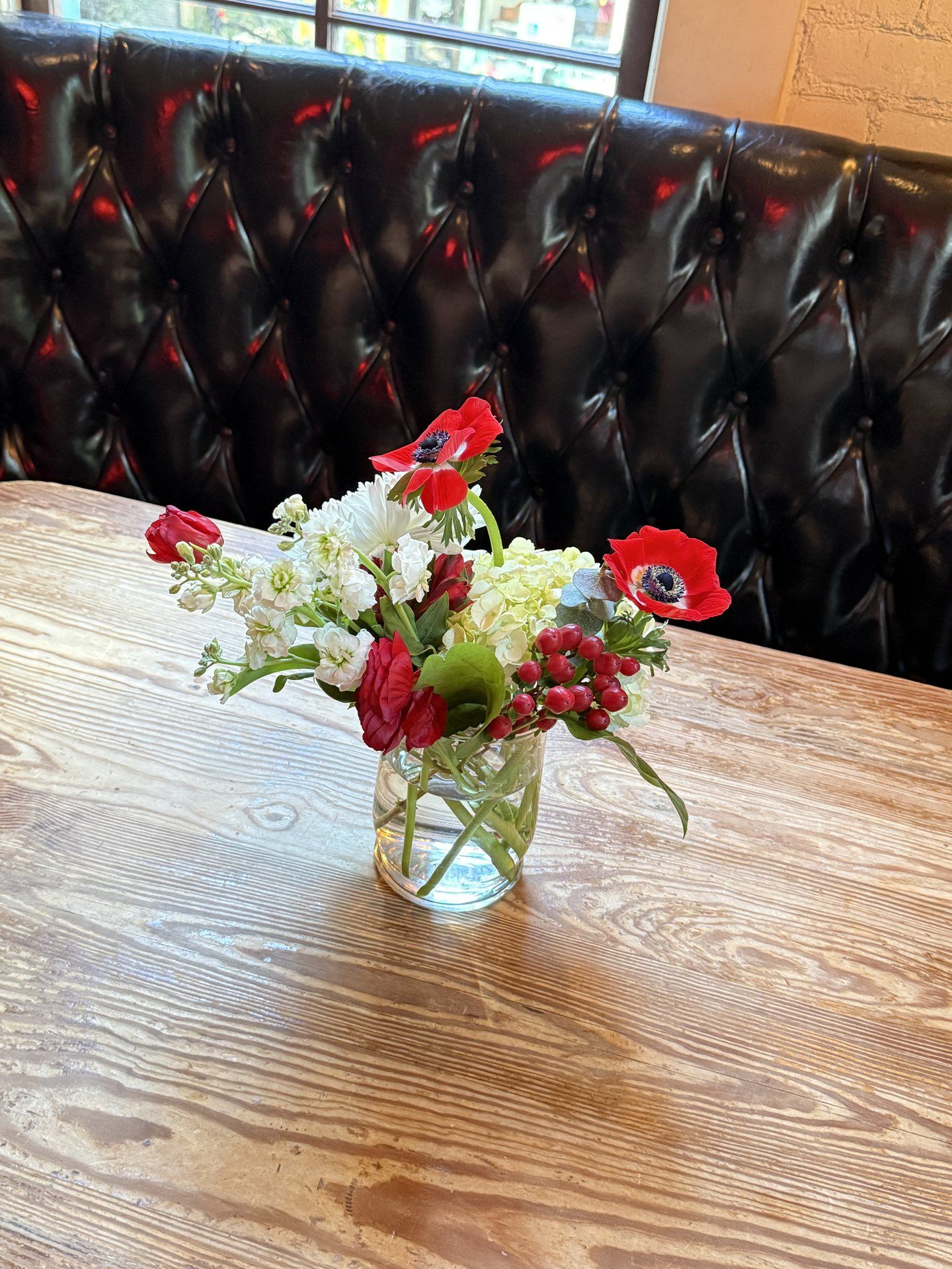 Red anemones, ranunculus, and hypericum berries with white stock — petite florals that bring personality to restaurant and venue tables.