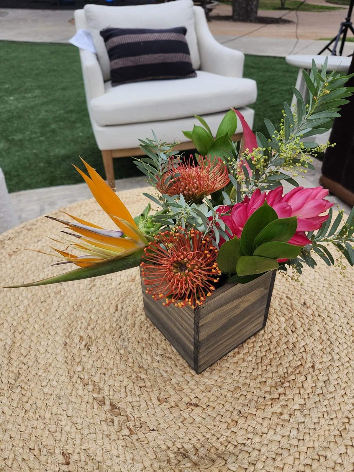 Birds of paradise, pincushion protea, and pink ginger in a wooden box — a tropical vignette for an outdoor lounge.