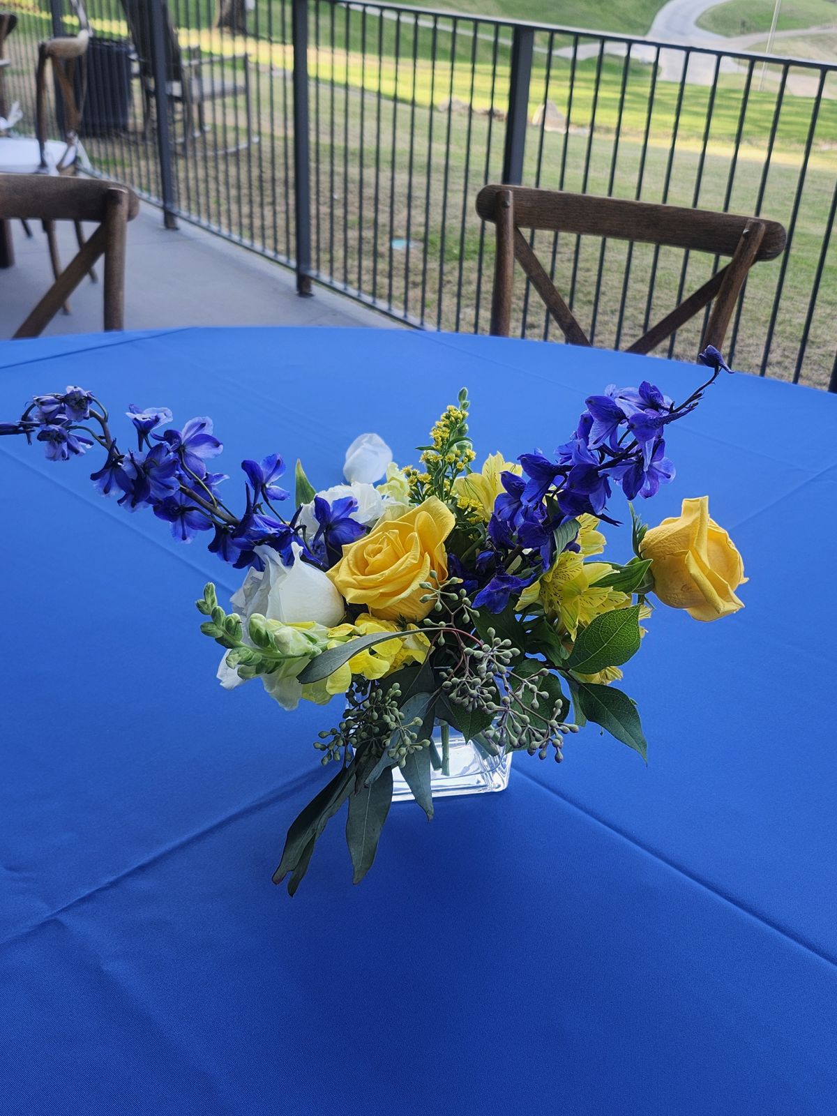 Blue delphinium and yellow roses in a compact arrangement — built to match brand colors down to the linen.