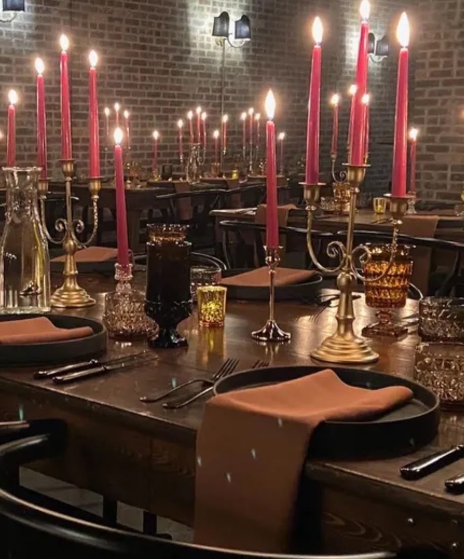 Brass candelabras with crimson tapers running down dark wood tables — timeless drama and candlelight warmth.