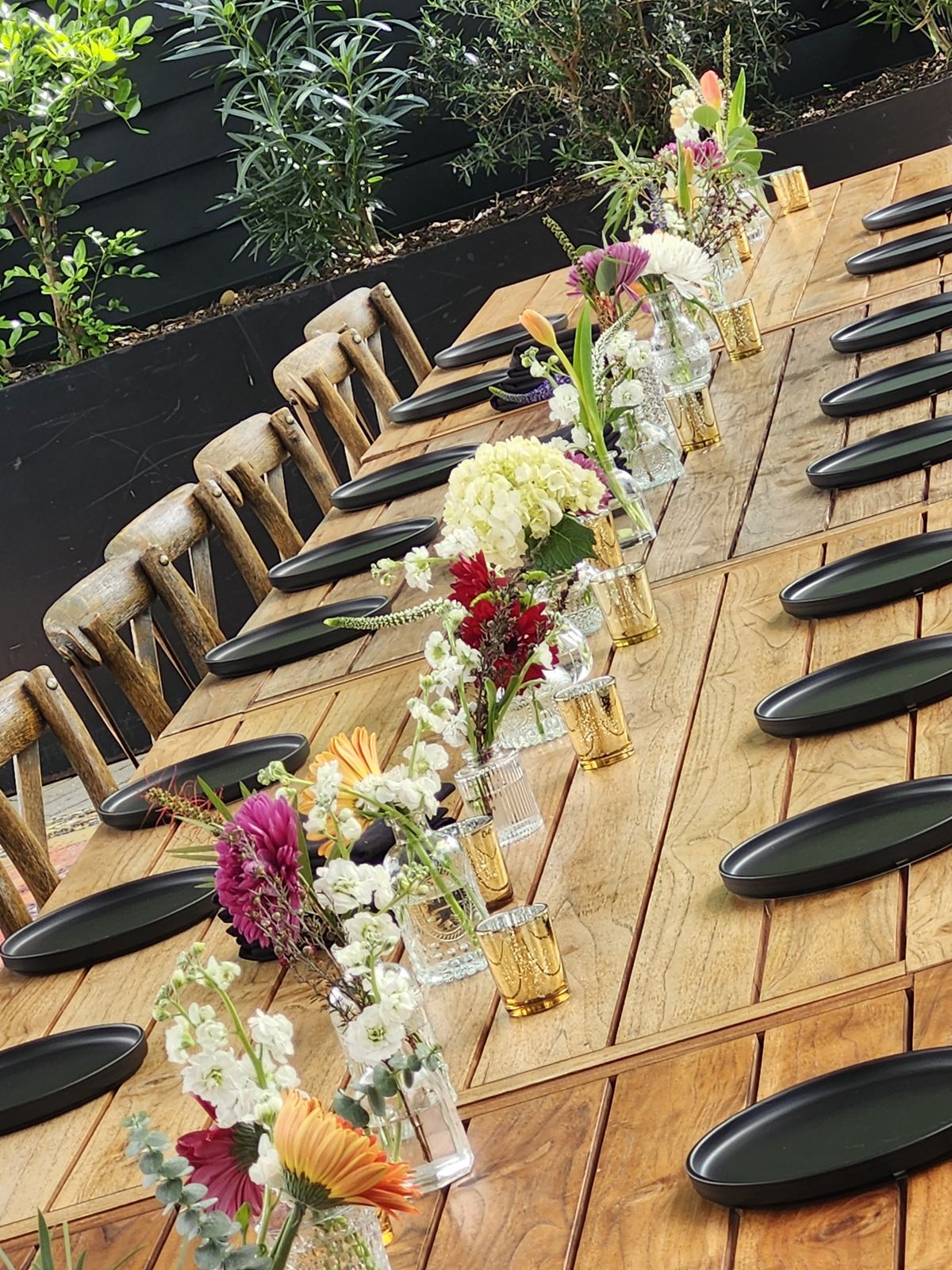Bud vases and low blooms running the length of a farm table — a floral runner guests dine beside, not around.