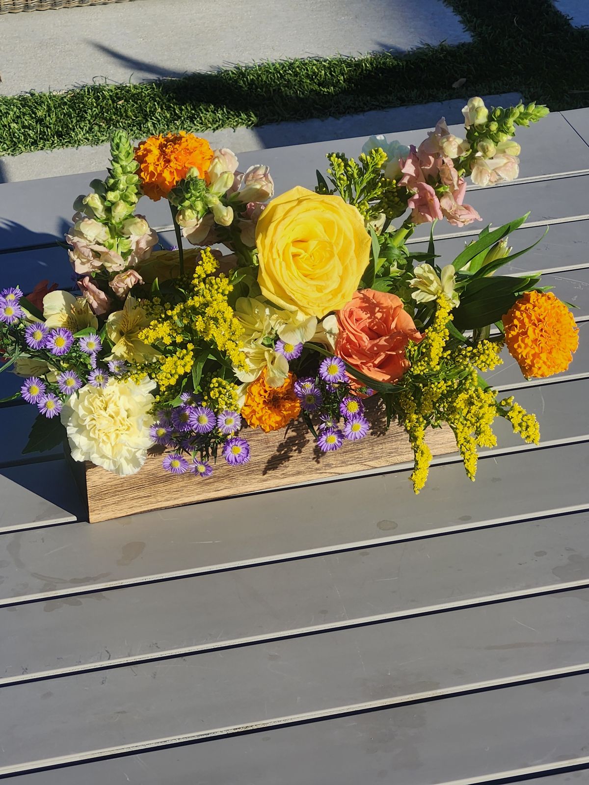 Golden ranunculus, marigolds, and violet asters in a long wooden box — warm Texas color for patio tables.