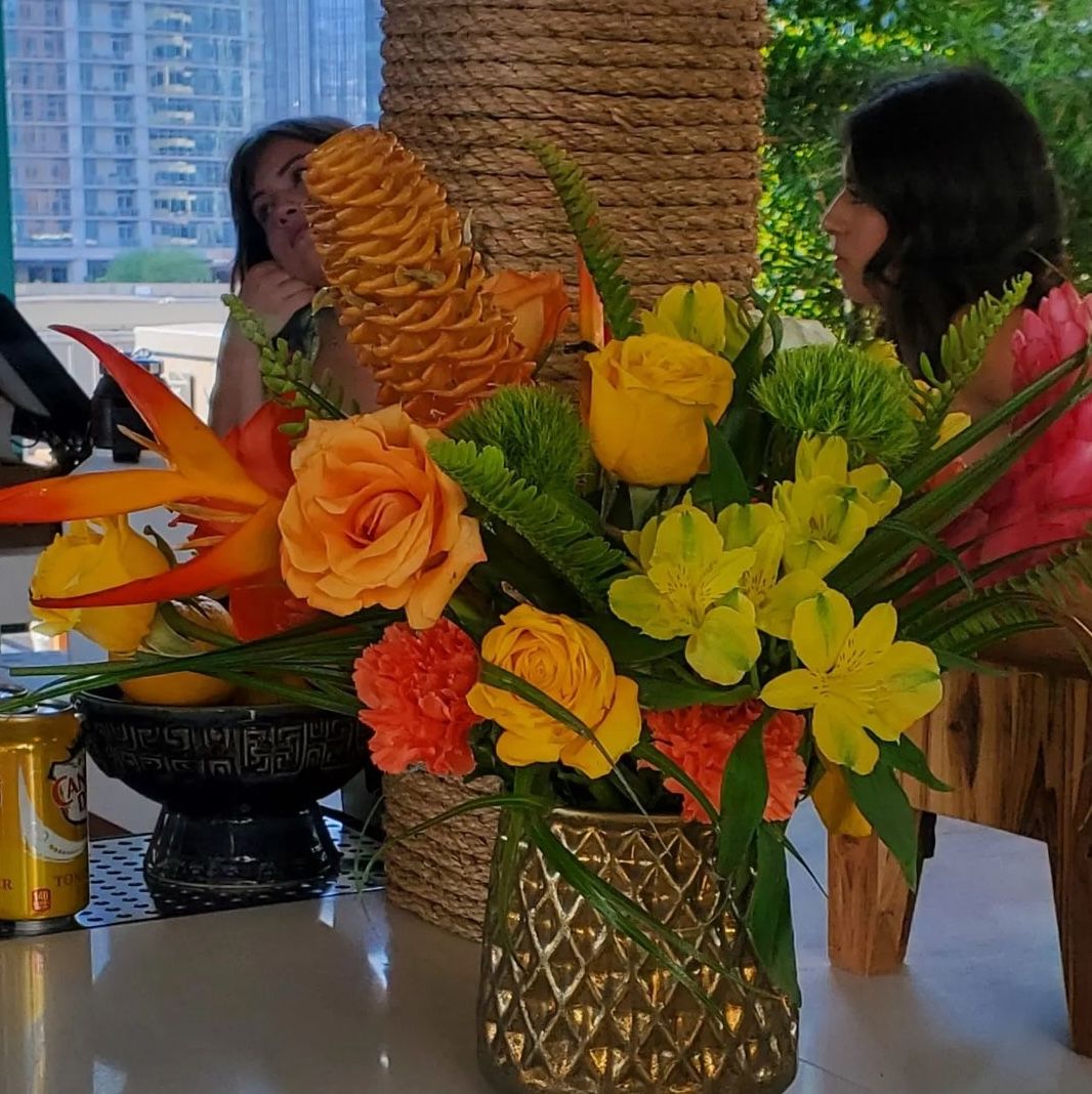 Heliconia, yellow roses, and alstroemeria in a gold vase at a rooftop happy hour above downtown Austin.