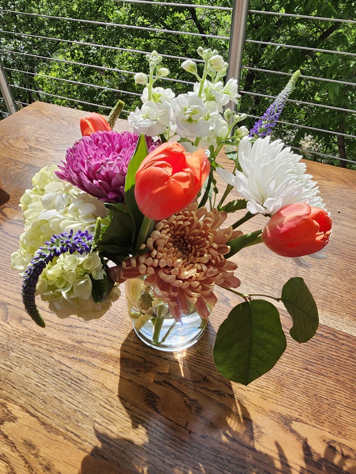 Coral tulips, chrysanthemums, and white stock in a footed glass vase — a fresh study in spring color.