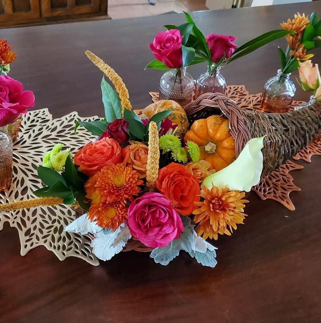 A cornucopia spilling roses, dahlias, and pumpkins in autumn tones — seasonal florals for a Thanksgiving gathering.