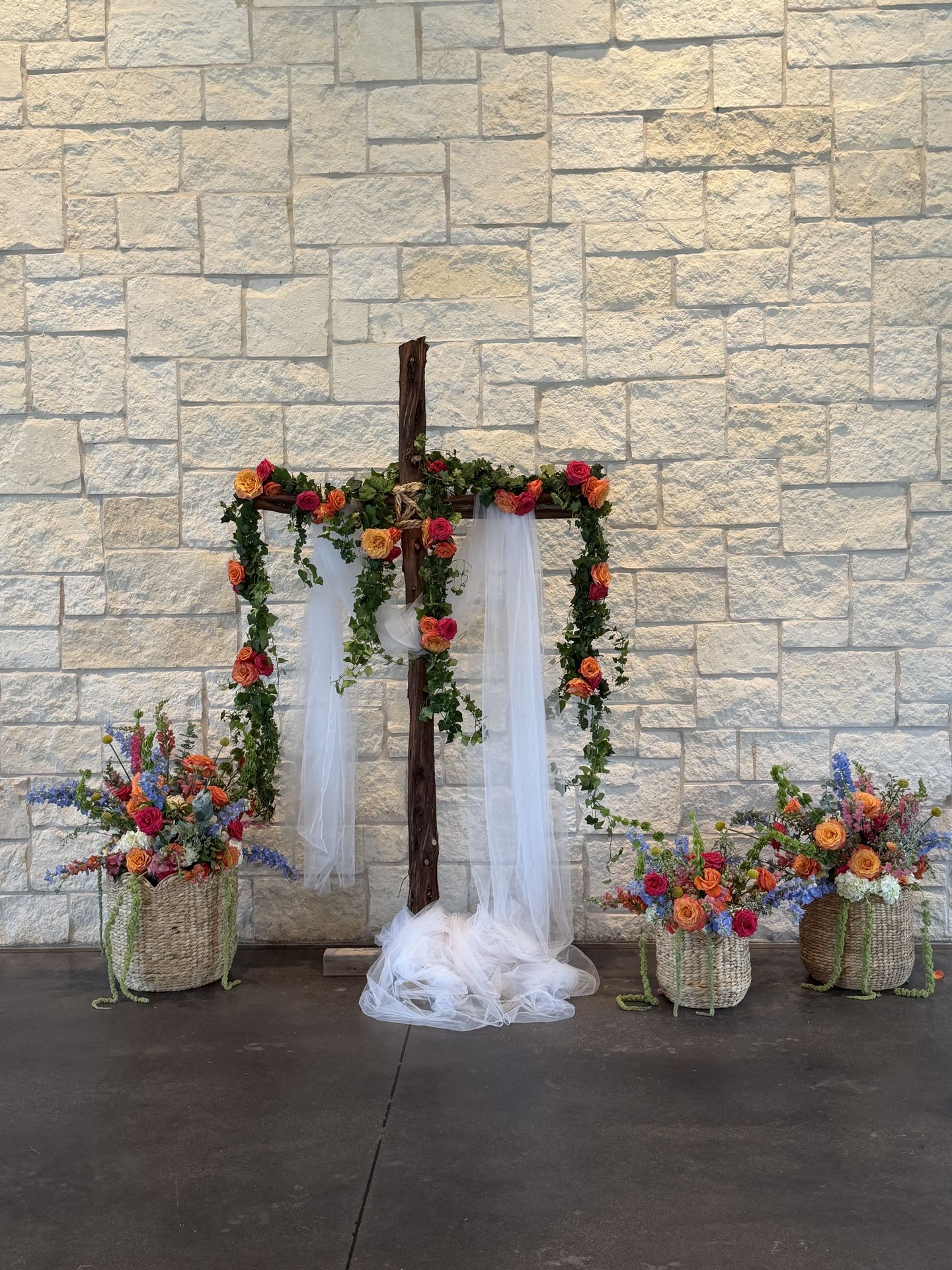 Wedding ceremony altar cross wrapped in ivy garland and coral roses at an Austin stone chapel