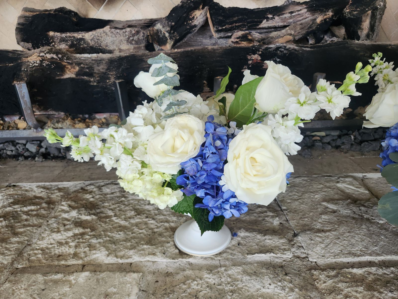 White roses, stock, and blue hydrangea in a footed white compote — romantic, refined, and endlessly elegant.