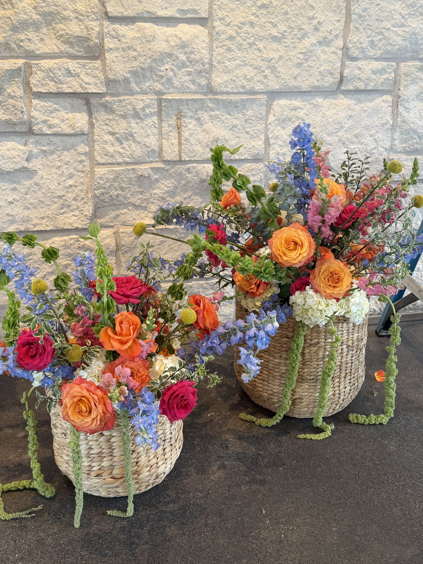 Woven baskets of orange roses and blue delphinium flanking a wedding ceremony