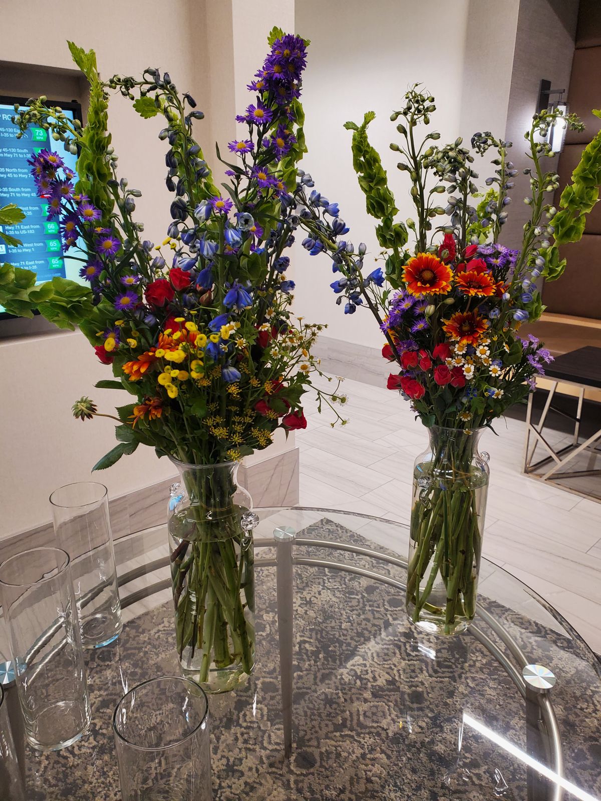 Loose delphinium, bells of Ireland, and firewheel gathered in tall vases — approachable, Austin-native charm for a networking evening.